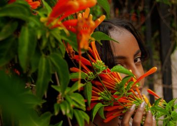 Girl looks towards camera from behind a flower with orange petals